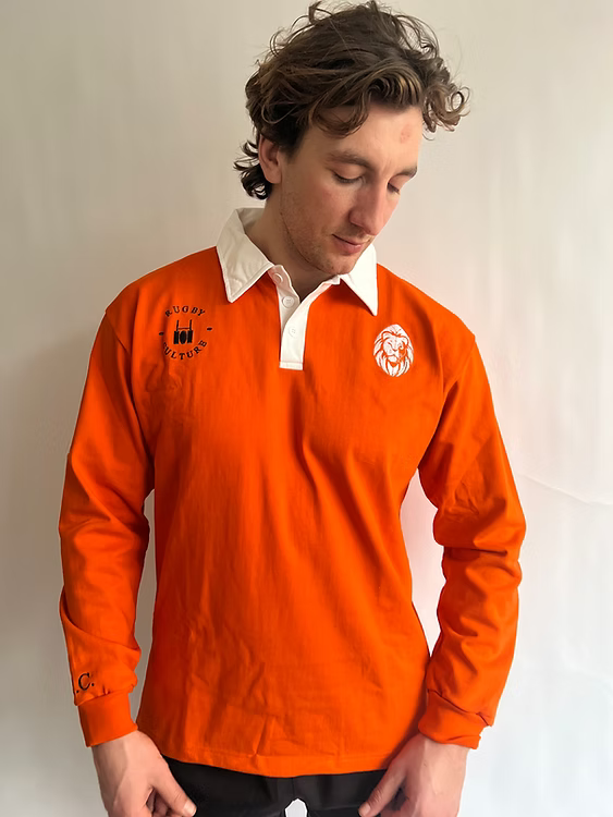 Man wearing an orange rugby shirt with a logo on a plain background