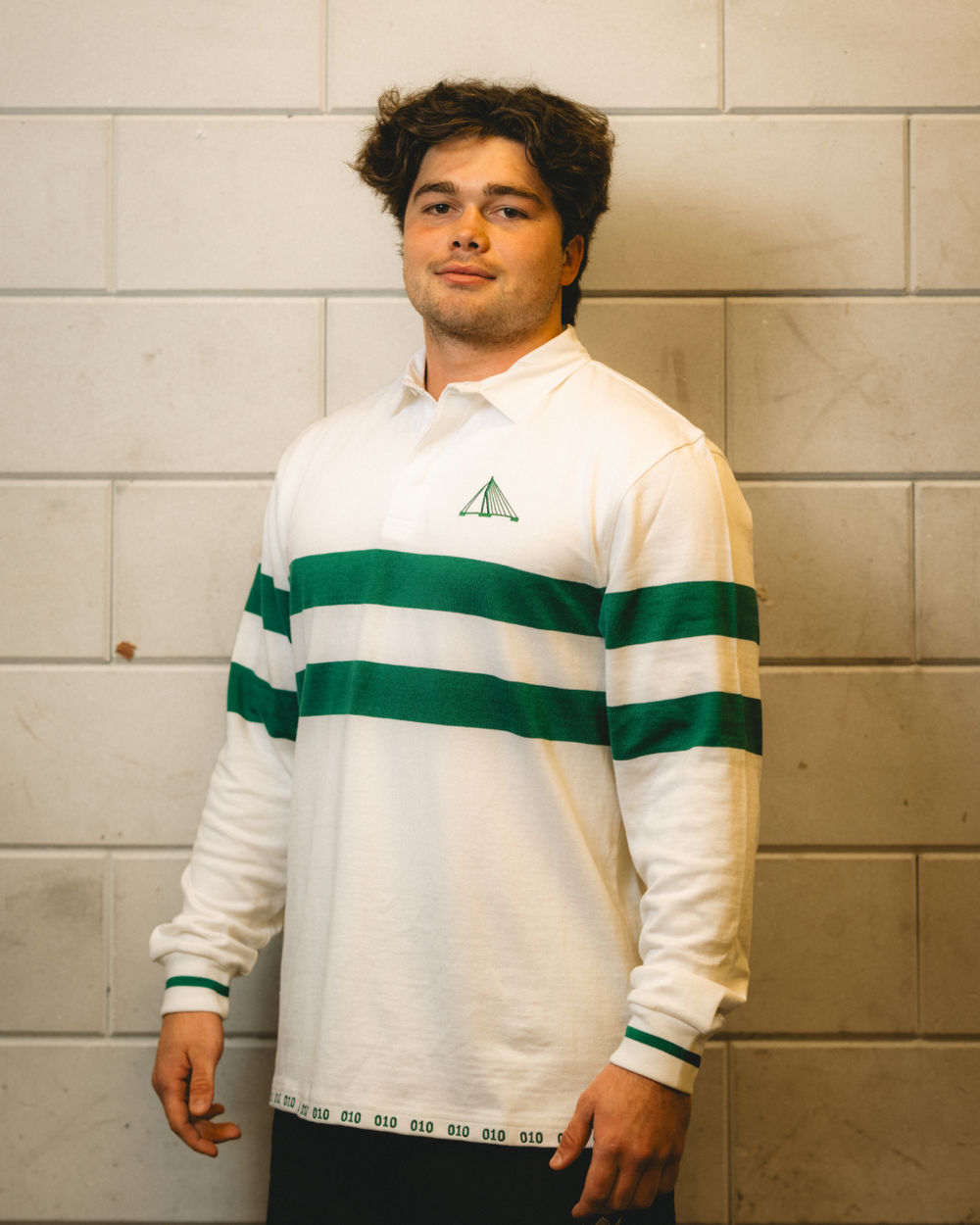 Male model wearing the Rugby Culture Rotterdam Heritage Rugby Polo against a white brick wall