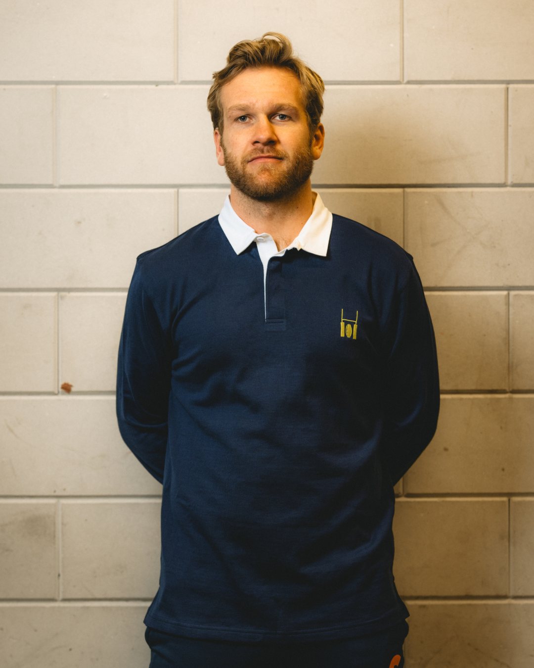 Male model wearing the Rugby Culture Navy Blue Rugby Polo against a white brick wall