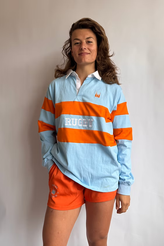 Female model wearing the Rugby Culture Sky Blue & Orange Rugby Polo with orange shorts, front view