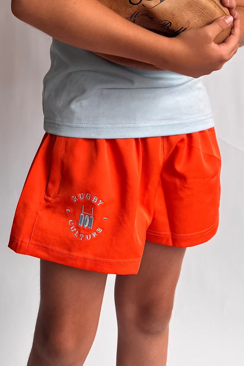 Close-up of orange Rugby Culture kids' scrum shorts, child holding a rugby ball