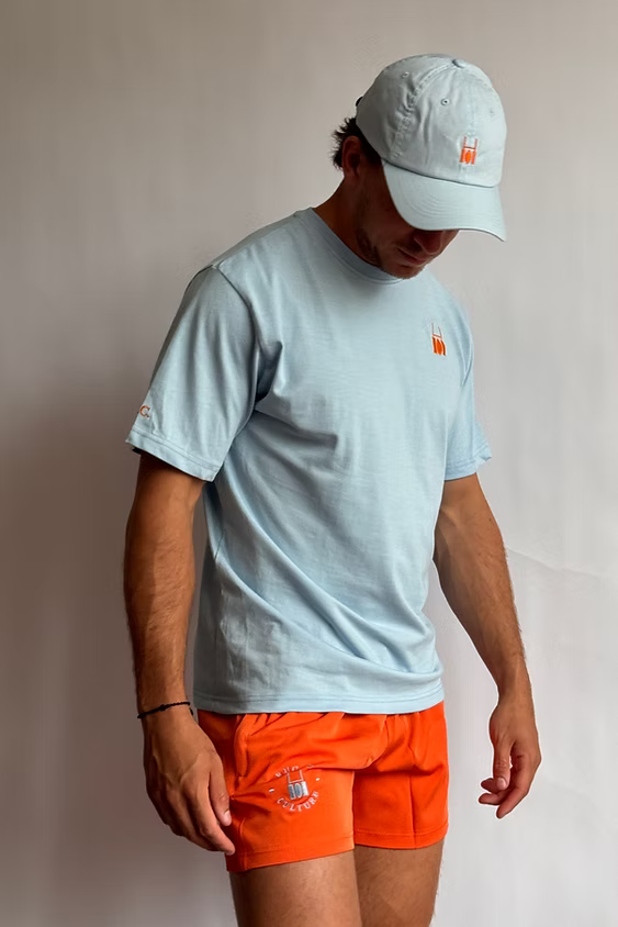 Rugby Culture Baby Blue Back Print T-Shirt worn with a cap and orange scrum shorts, front view