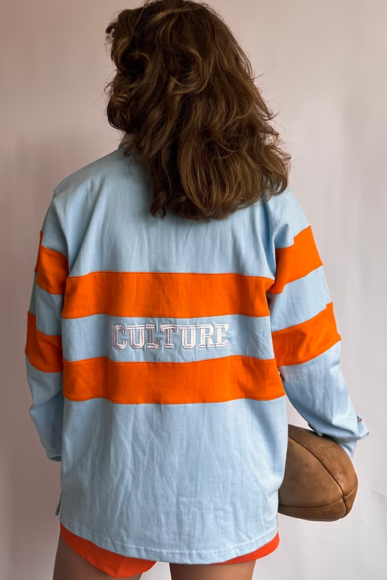 Female model wearing the Rugby Culture Sky Blue & Orange Rugby Polo, back view