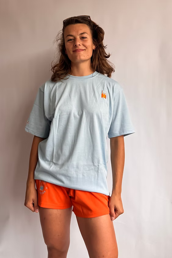 Rugby Culture Baby Blue Back Print T-Shirt worn by a female model with orange shorts, front view