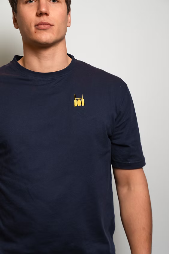 Rugby Culture Blue Basic Logo T-Shirt worn by a male model, close-up of the embroidered crest