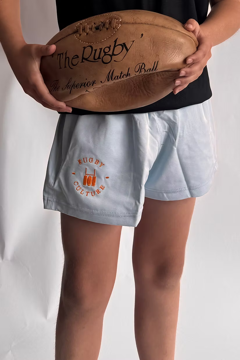 Close-up of Rugby Culture Kids Baby Blue Scrum Shorts, child holding a rugby ball
