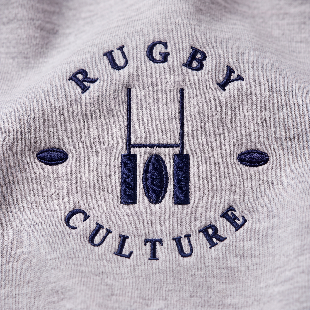 Close-up of the navy embroidered Rugby Culture goalpost emblem on grey cotton