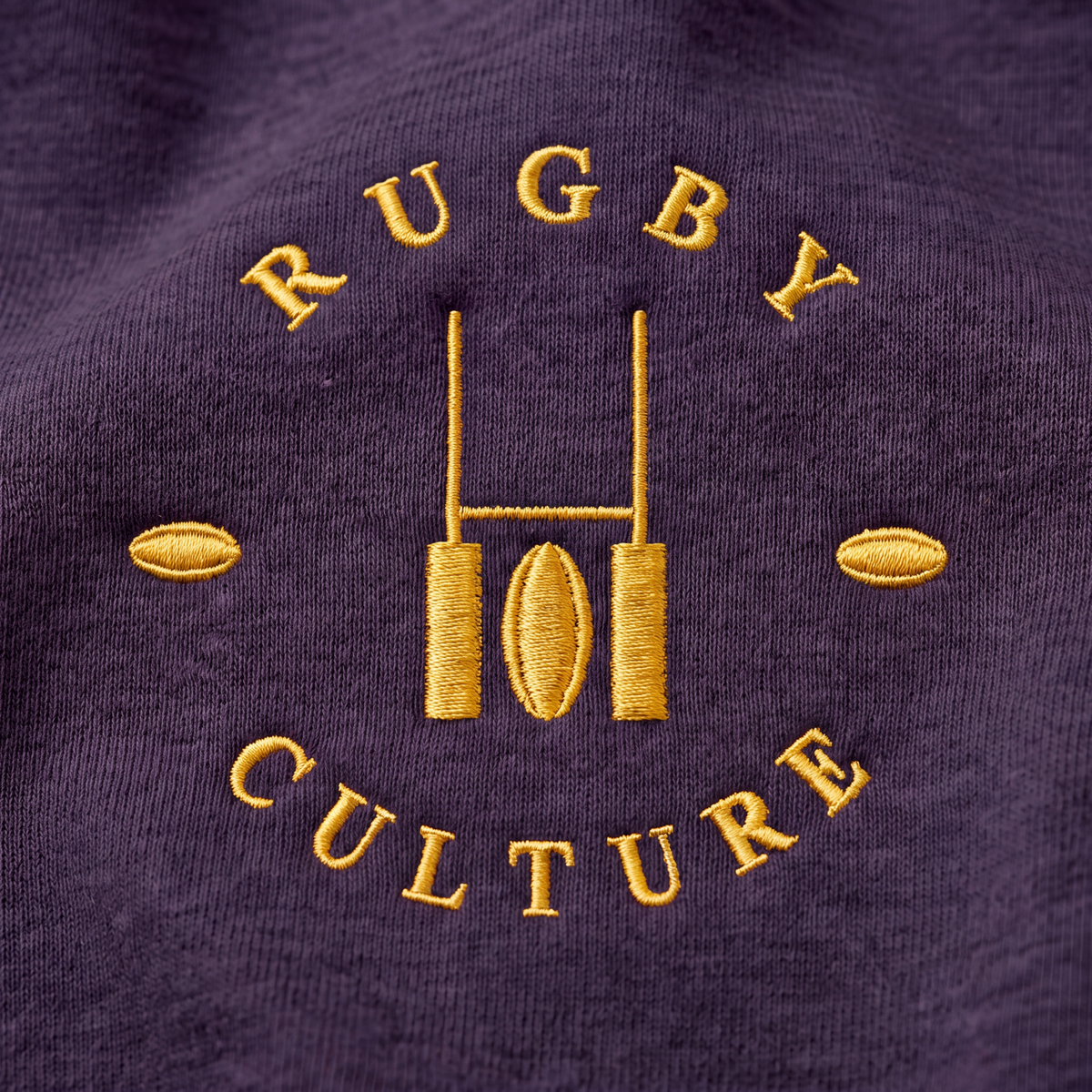 Close-up of the gold embroidered Rugby Culture goalpost emblem on navy cotton