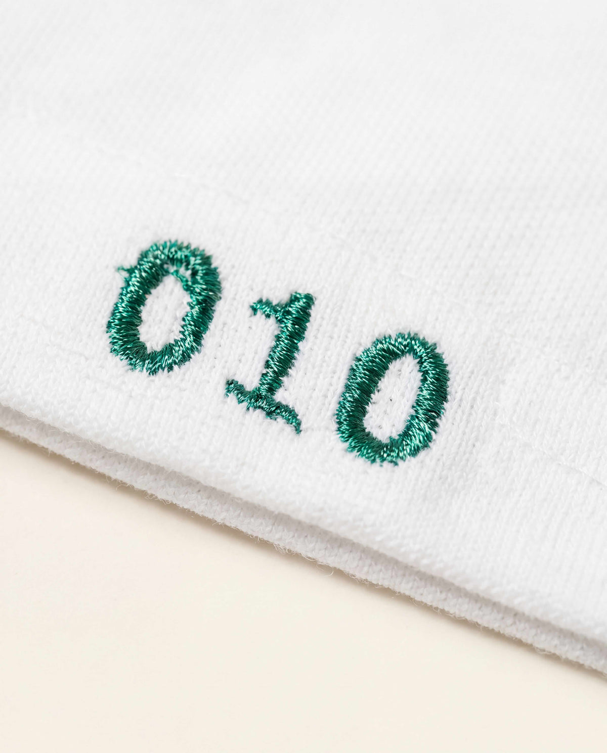 Close-up of the green '010' embroidery on the hem of the Rotterdam Heritage Rugby Polo